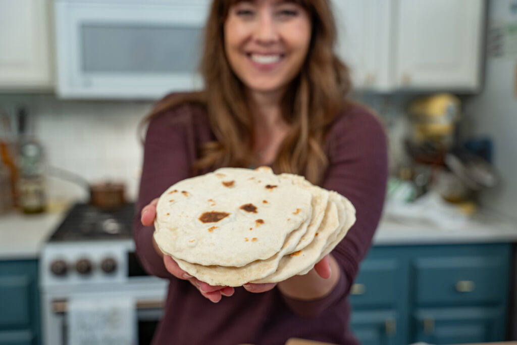 A woman standing in the kitchen holding a stack of sourdough tortillas.