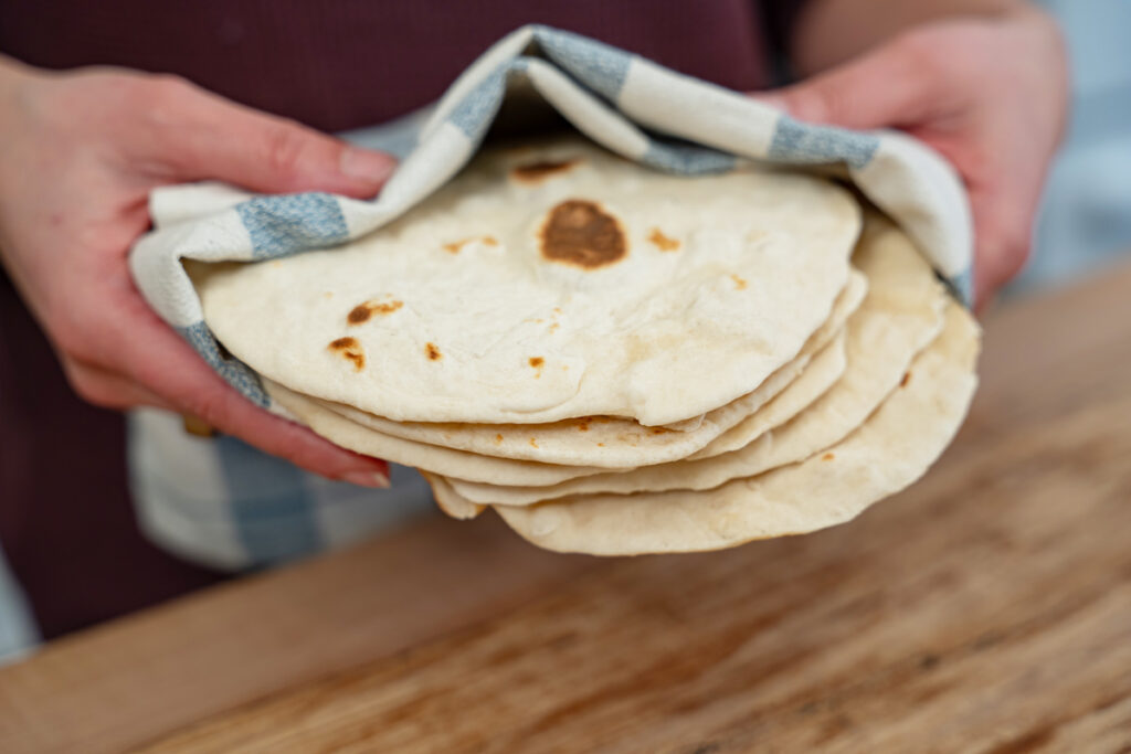 Sourdough flour tortillas in a stack being held by a woman's hands.