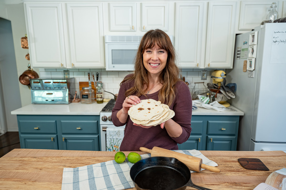 A woman standing in the kitchen holding a stack of sourdough tortillas.