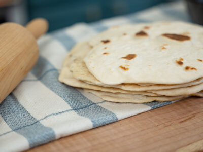 A stack of sourdough tortillas on a towel lined counter.