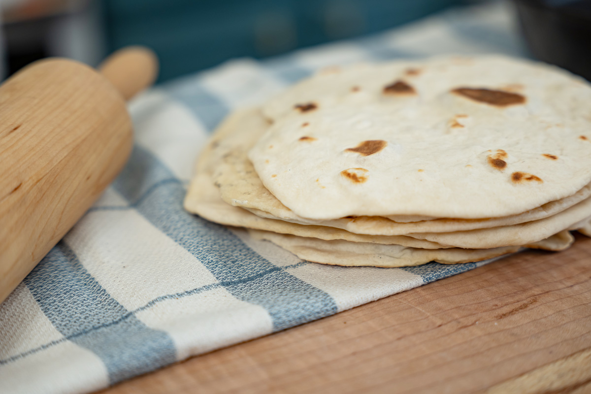 A stack of sourdough tortillas on a towel lined counter.