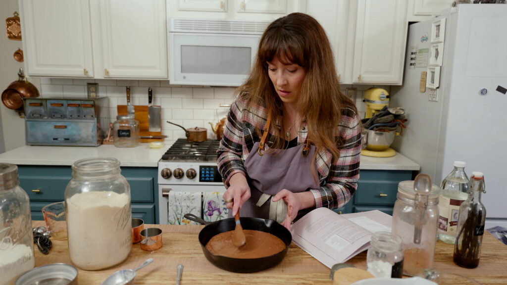 A woman spreading chocolate cake batter into a cast iron skillet.