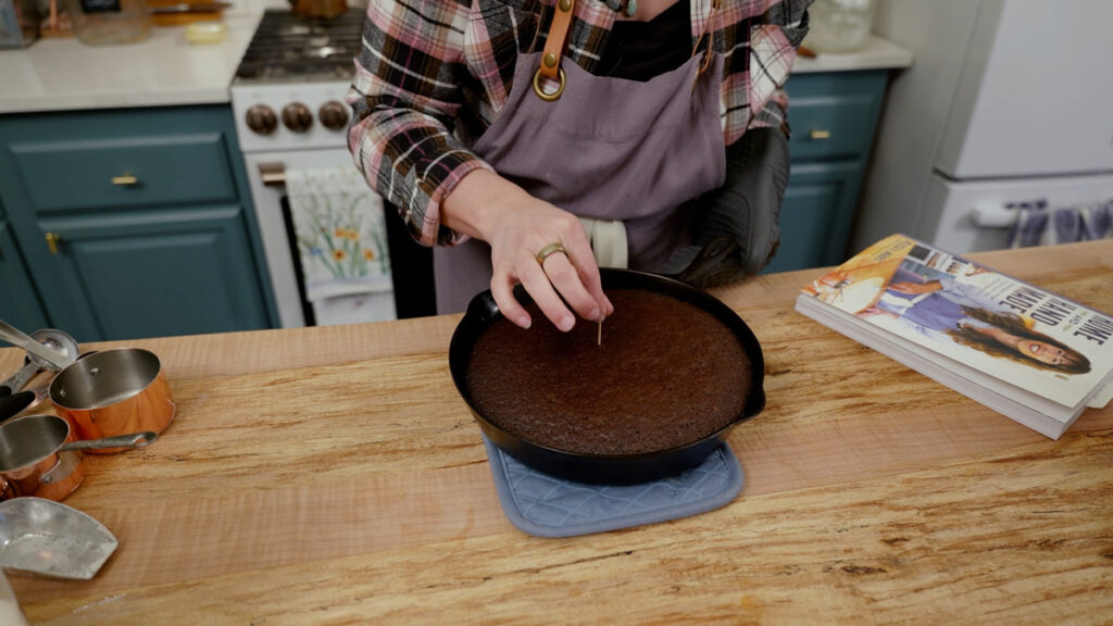 A woman testing a cake for doneness with a toothpick.