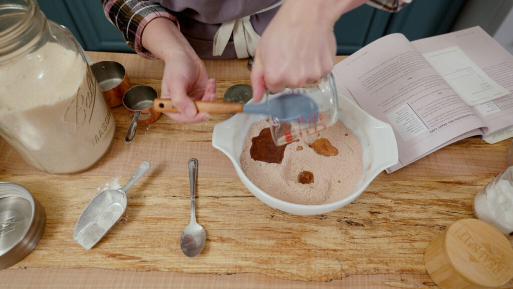 Ingredients for chocolate wacky cake being added to a bowl.