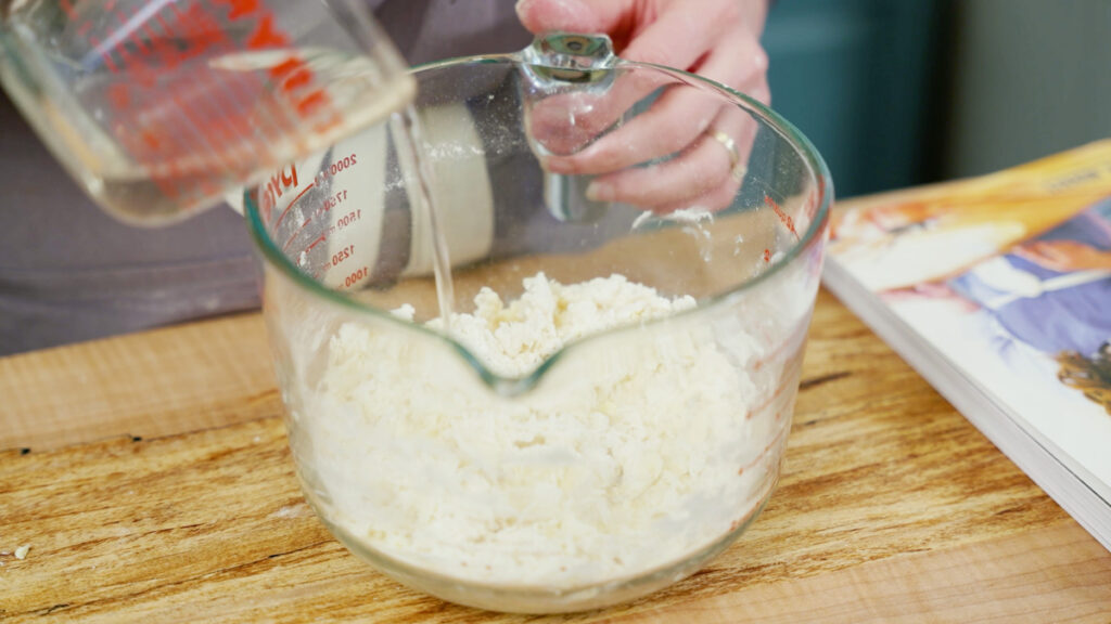 Water being poured into a bowl with flour and butter.