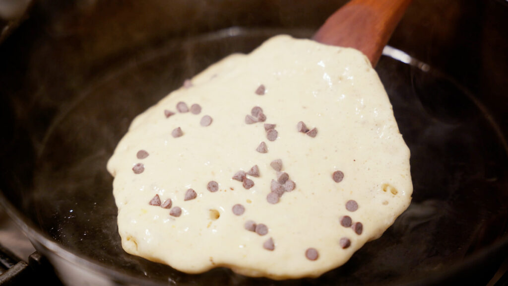 Sourdough discard pancake cooking in the pan with mini chocolate chips on top.