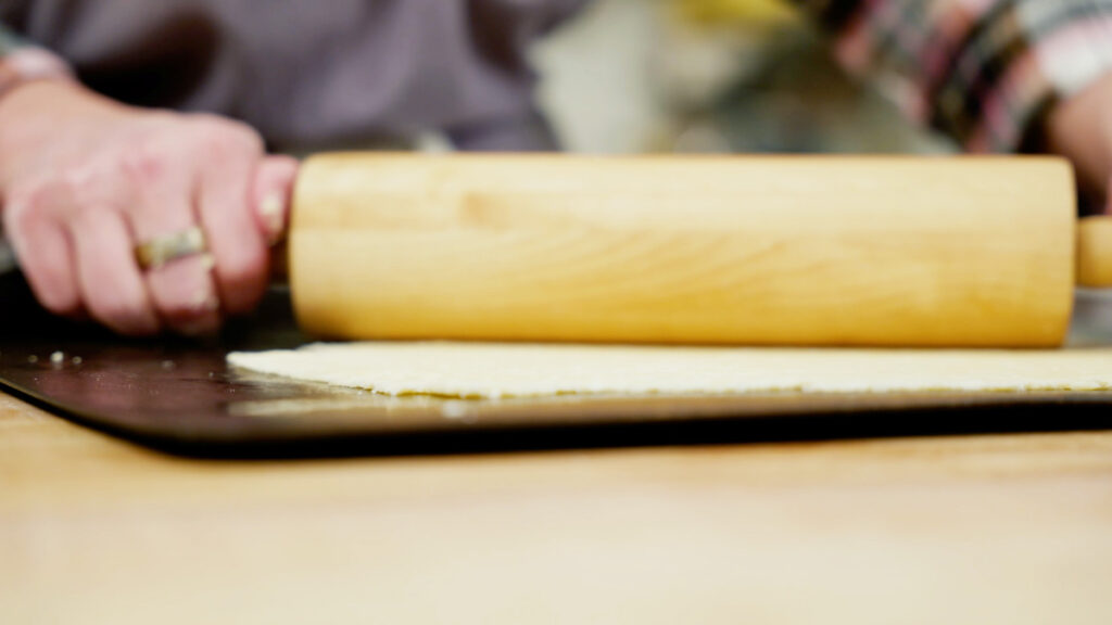 Cracker dough being rolled out very thin with a rolling pin.