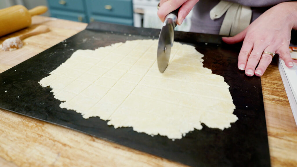 Homemade cracker dough being cut into squares with a pizza cutter.