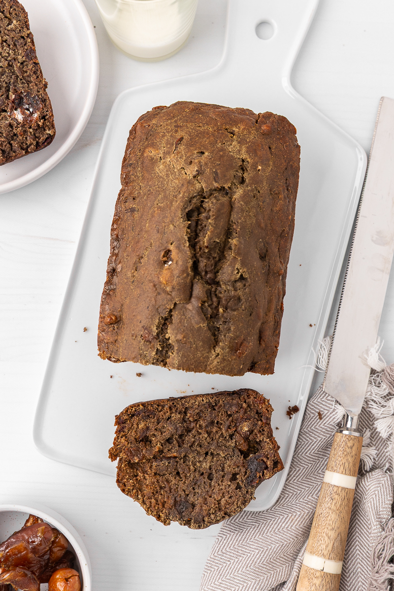 A loaf of date bread that's been sliced on a white serving platter.
