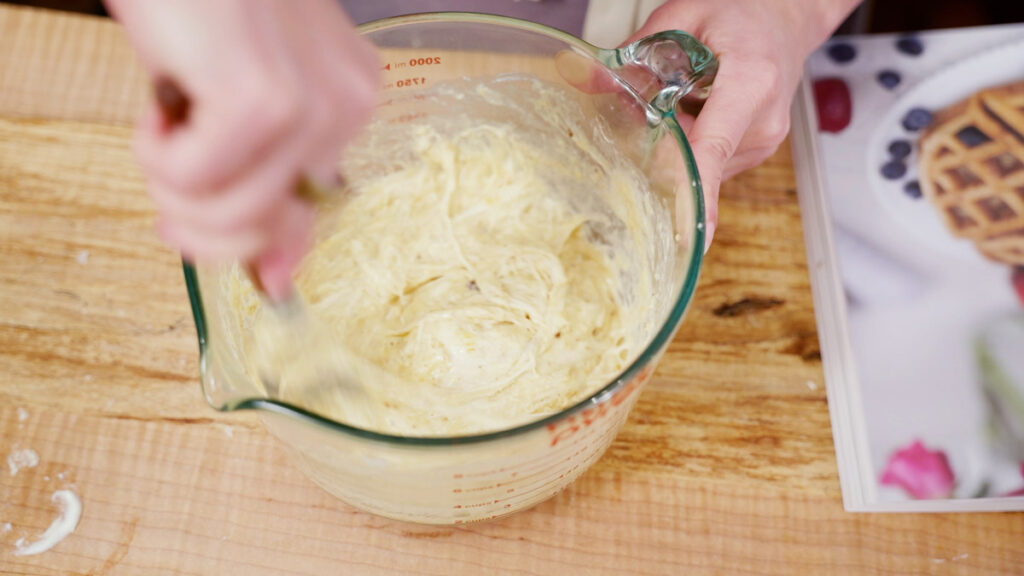 A mixing bowl with sourdough pancake batter being stirred together.