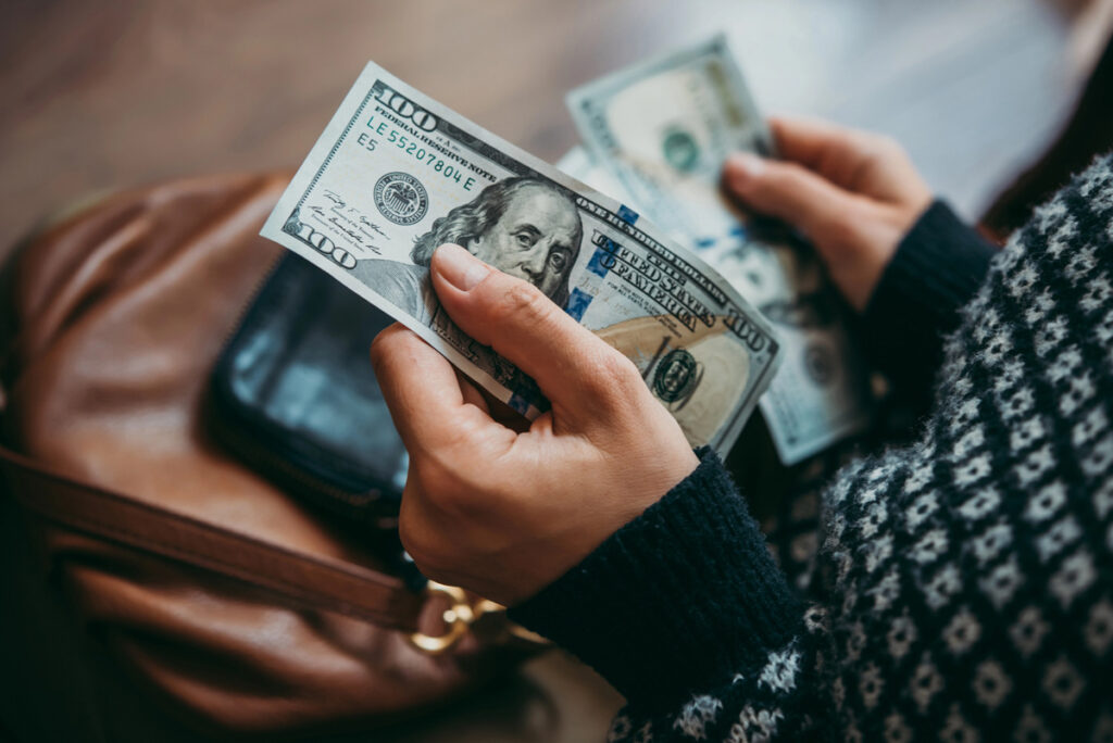 A woman holding hundred dollar bills with a purse in her lap.