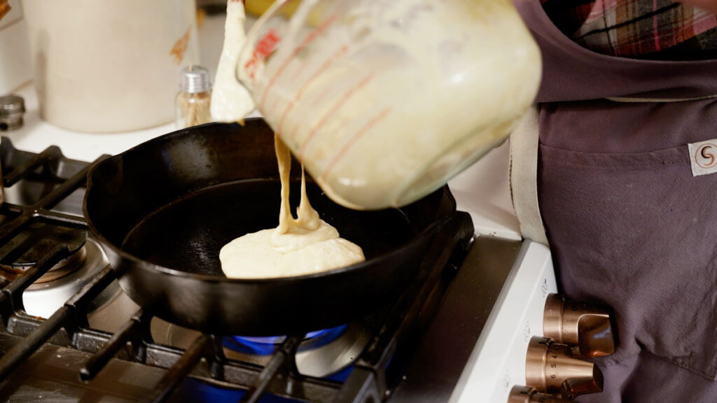 Sourdough pancake batter being poured into a hot cast iron skillet.