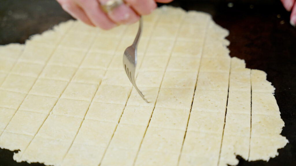 Homemade cracker dough being pricked with a fork.