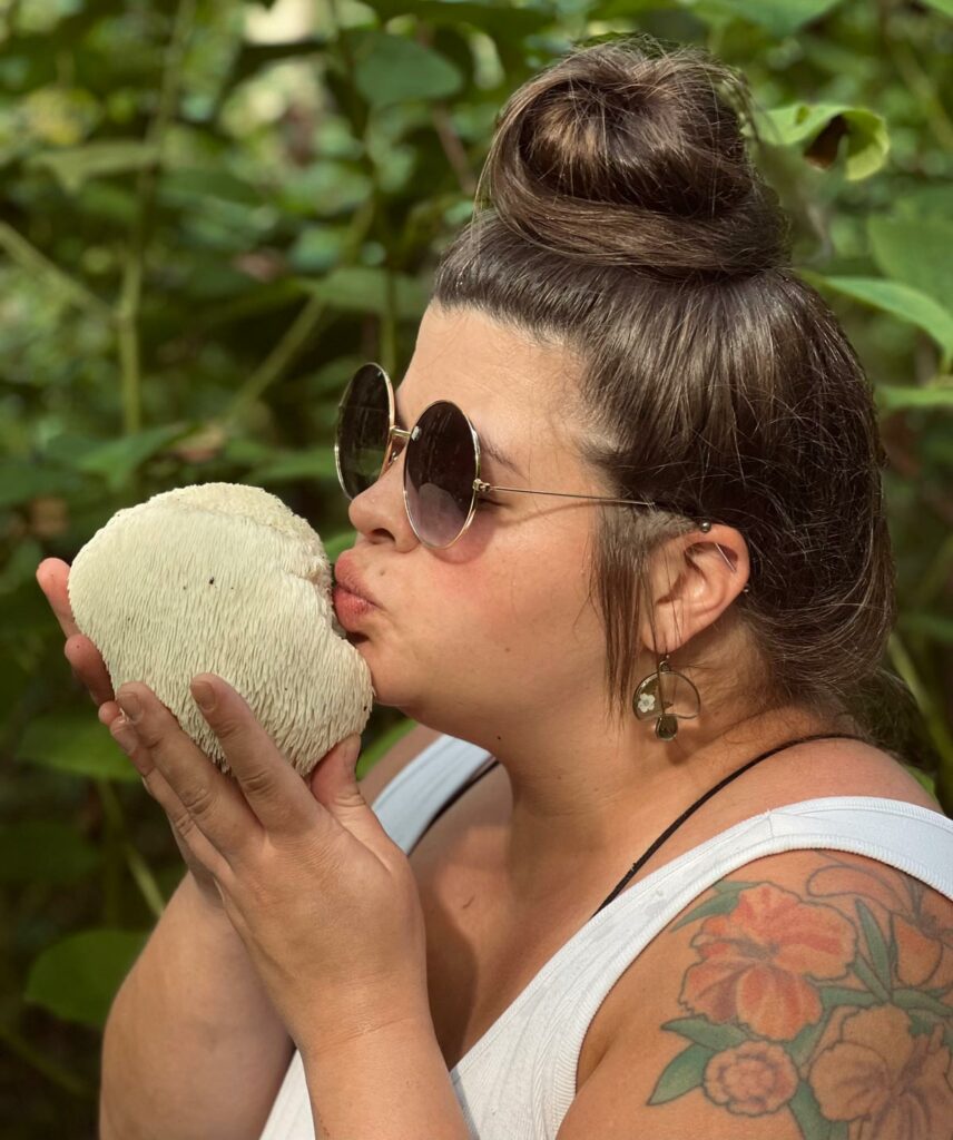 A girl with sunglasses on kissing a freshly harvested wild mushroom.