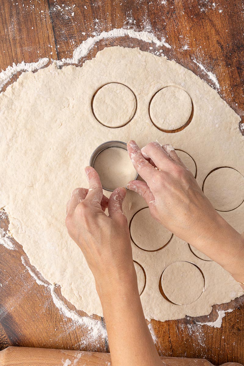 A woman's hands cutting biscuit dough with a biscuit cutter.