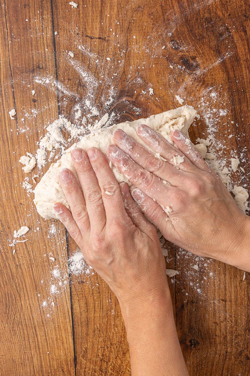 A woman's hands kneading biscuit dough on a floured wooden counter.