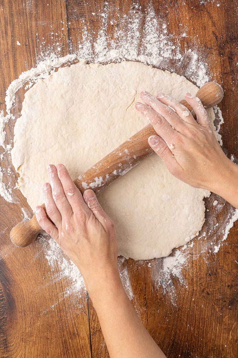 Woman's hands rolling out biscuit dough with a wooden rolling pin.