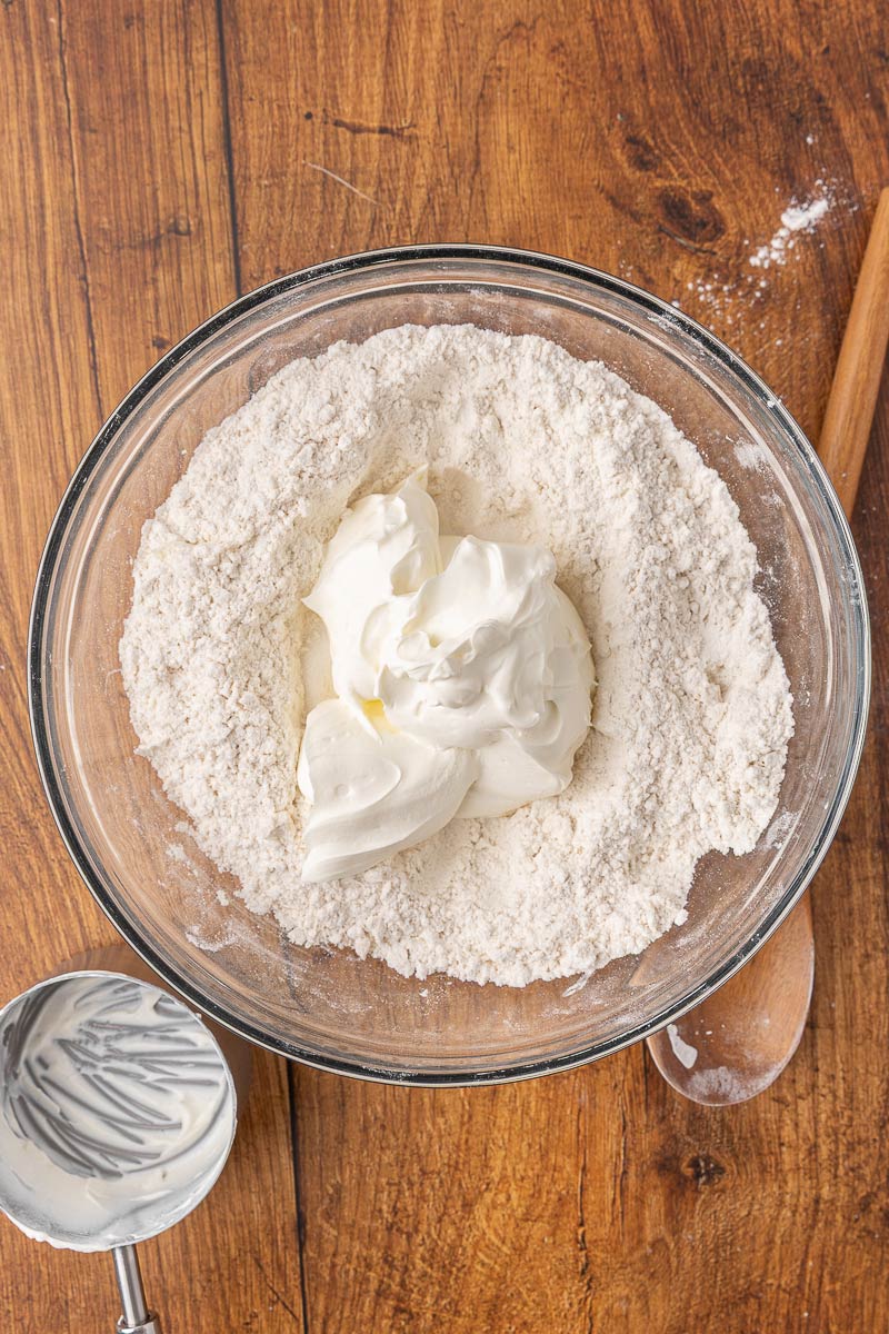 Sour cream being added to a bowl of dry ingredients for homemade sour cream biscuits.