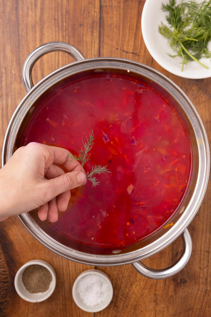 Adding fresh dill to a stock pot full of traditional Ukranian borscht