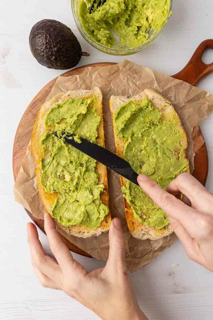 Mashed avocado being spread on two pieces of toast.