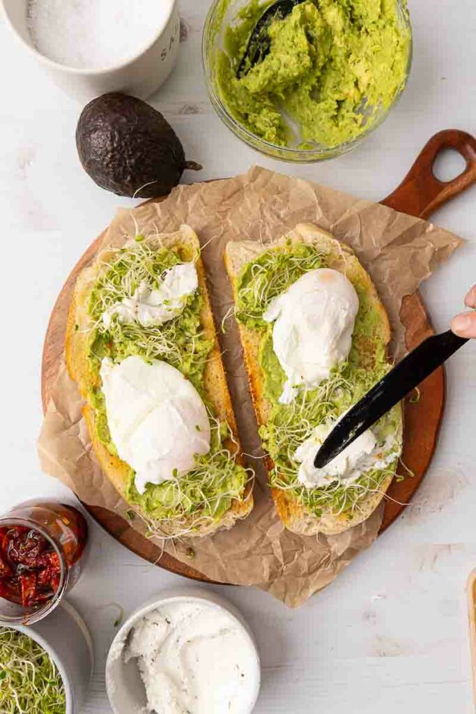 Goat cheese being spread onto two pieces of avocado toast.