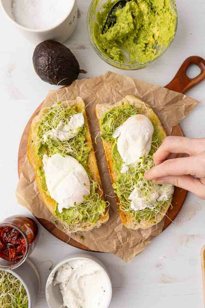 Herbs being sprinkled onto avocado toast.