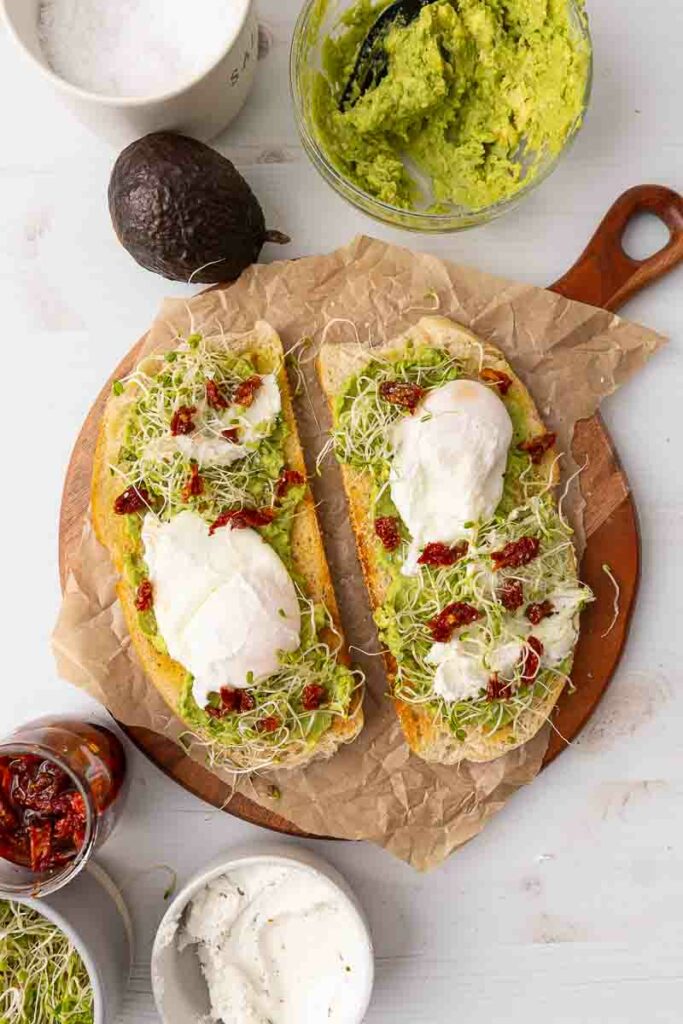 Two pieces of avocado toast with poached eggs and goat cheese and marinated sundried tomatoes.