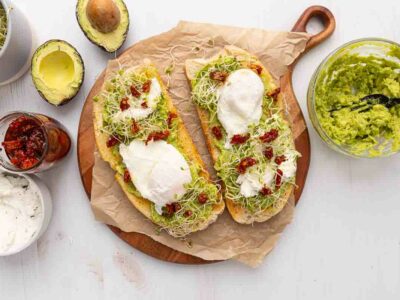 Two pieces of avocado toast with poached eggs and goat cheese and marinated sundried tomatoes.