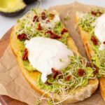 Two pieces of avocado toast with poached eggs and goat cheese and marinated sundried tomatoes.