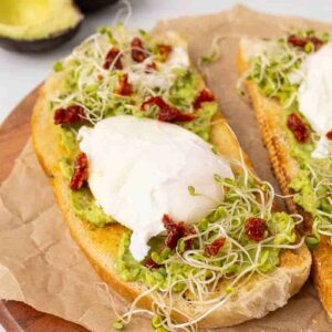 Two pieces of avocado toast with poached eggs and goat cheese and marinated sundried tomatoes.
