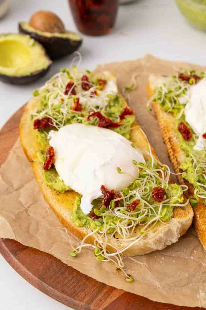 Two pieces of avocado toast with poached eggs and goat cheese and marinated sundried tomatoes.