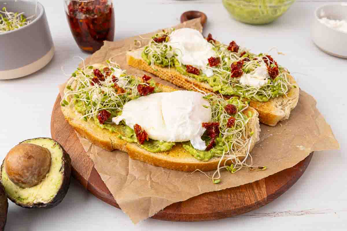 Two pieces of avocado toast with poached eggs and goat cheese and marinated sundried tomatoes.