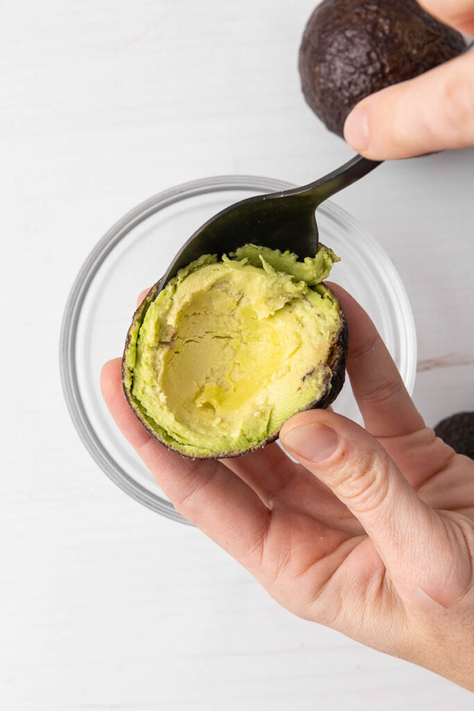 Scooping the flesh of an avocado out with a spoon.