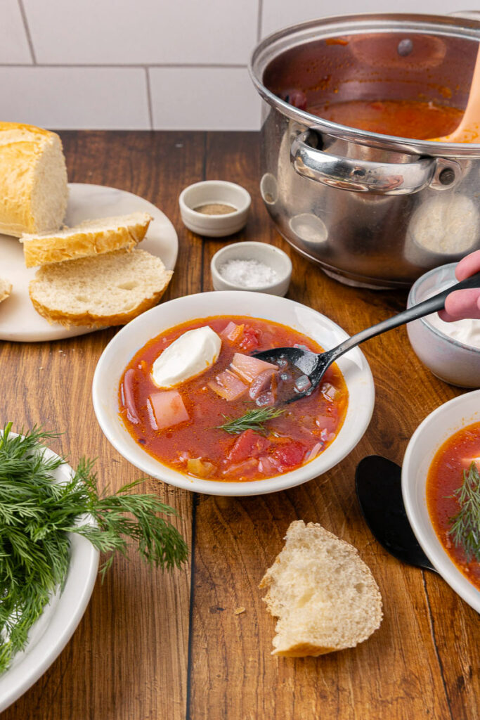 A spoon dipping into a bowl of traditional Ukranian borscht with slices of bread in the background.