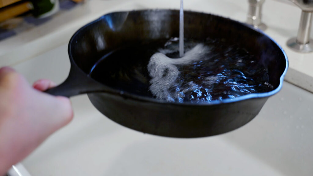 A cast iron pan being run under water.