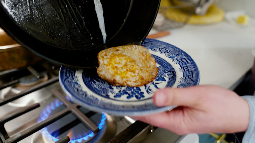 An egg being plated onto a blue plate.