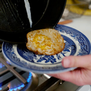 An egg being plated onto a blue plate.