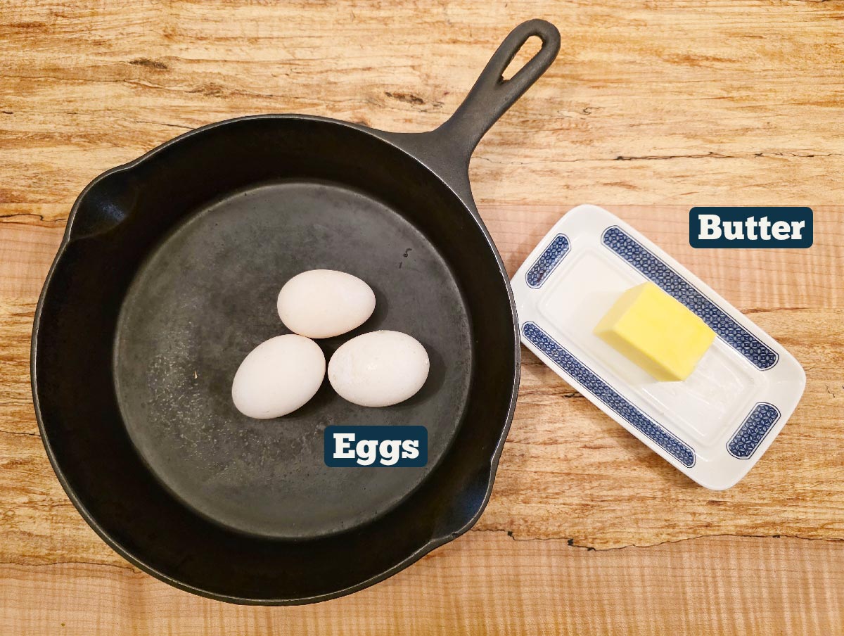 A cast iron pan with eggs and a stick of butter.