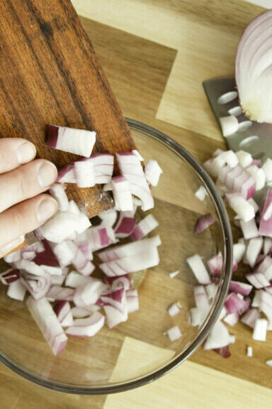 Wooden bench knife scooping onions up and putting them into a bowl.