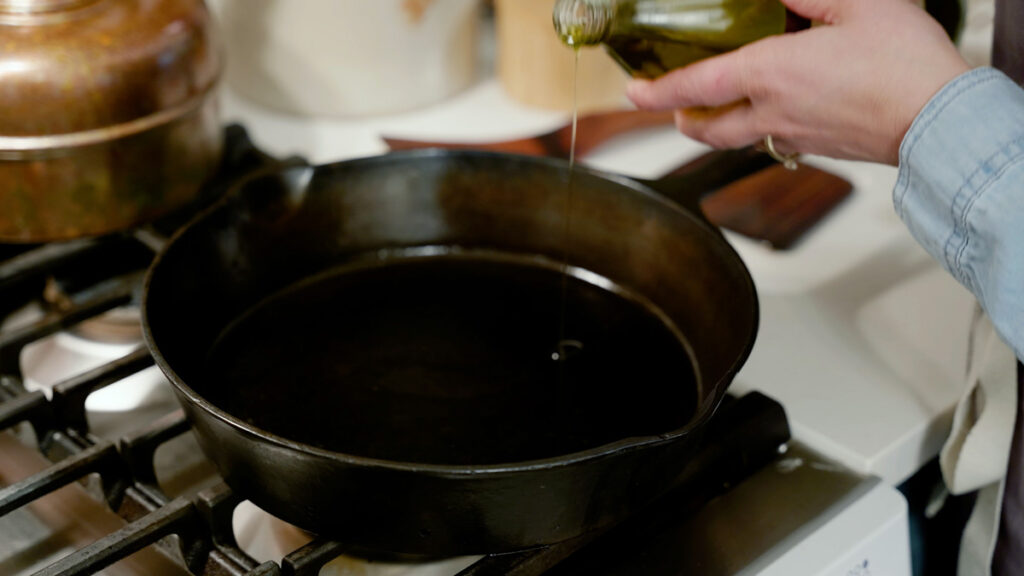 Oil being poured into a cast iron skillet.