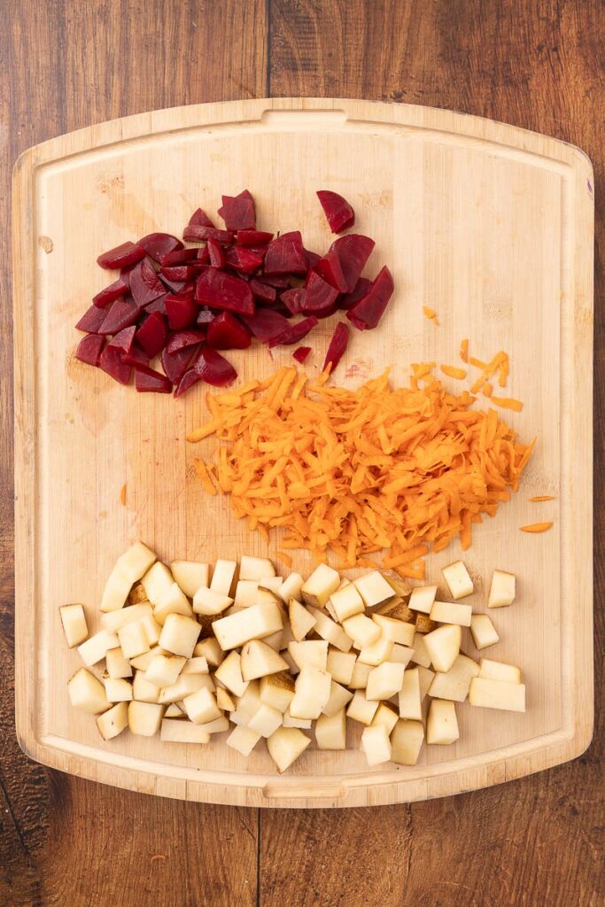 Diced beets, potatoes, and shredded carrots on a cutting board ready for traditional Ukranian borscht.