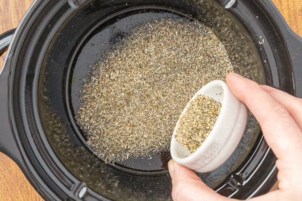 Pouring herbs into oil to make an herbal infusion in a crockpot.