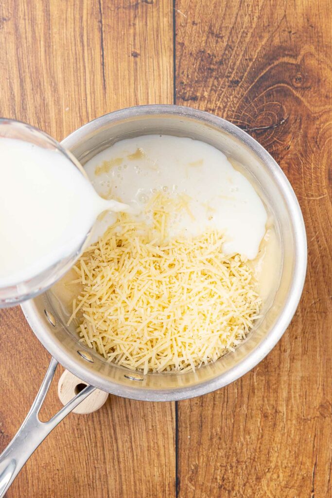 Pouring cream over grated parmesan in a saucepan to make Alfredo sauce.