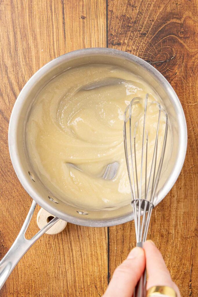 A hand whisking Alfredo sauce in a saucepan.