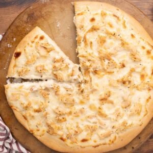 Baked chicken Alfredo pizza on a pizza stone with a slice missing.