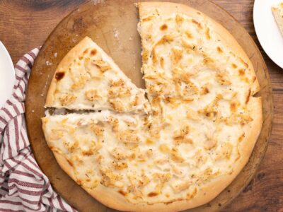 Baked chicken Alfredo pizza on a pizza stone with a slice missing.