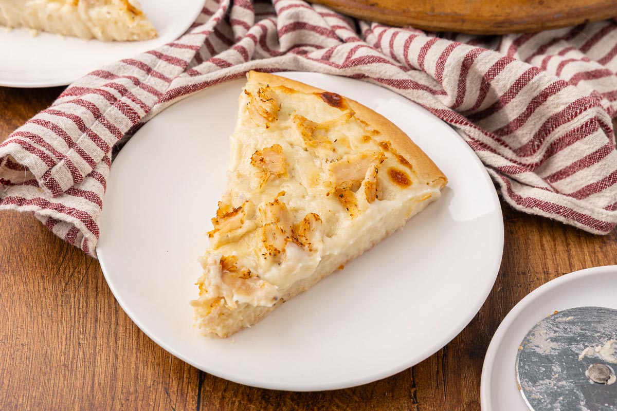 A slice of chicken Alfredo pizza on a white plate.