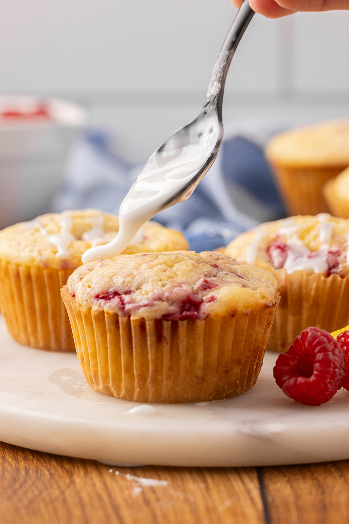 A spoon drizzling lemon glaze over a raspberry cream cheese muffin.