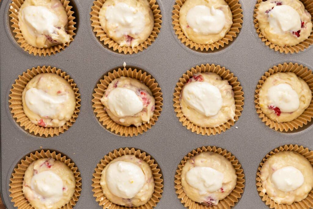 Raspberry muffin batter and cream cheese filling in a muffin tin.
