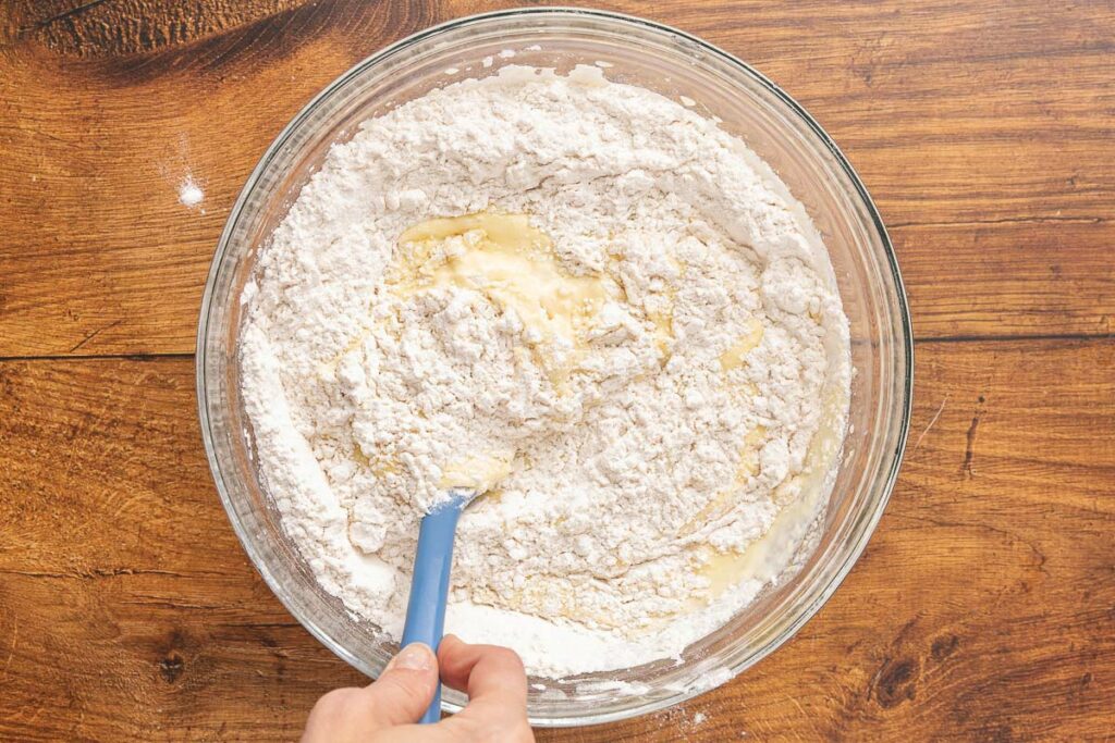 A hand holding a spatula folding the wet and dry muffin ingredients together.